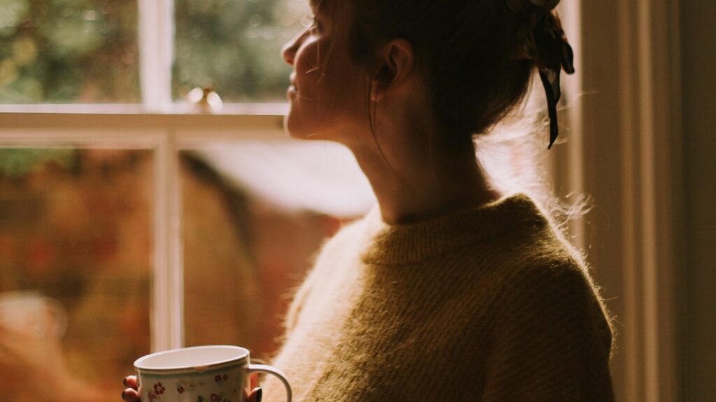 A woman by a window looking away, evoking the quiet emotional distance phubbing creates in a marriage