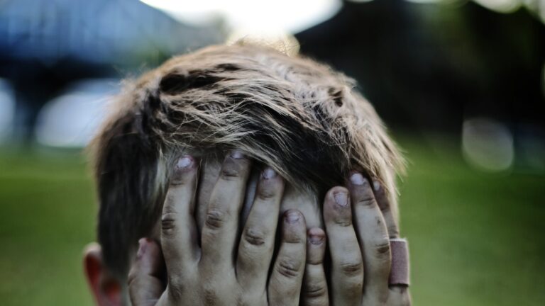 Anxious young boy sitting with his face covered