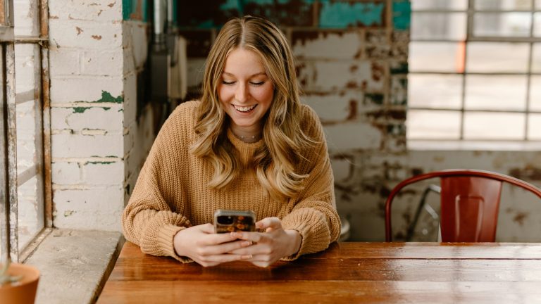 Woman sitting at a table looking at her phone, dating with anxiety