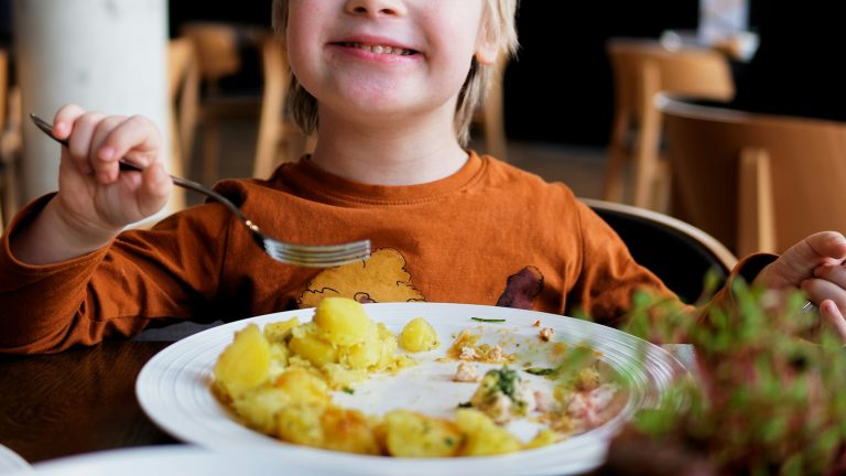 Little boy sitting at a table with a plate of food, a common picky eating moment