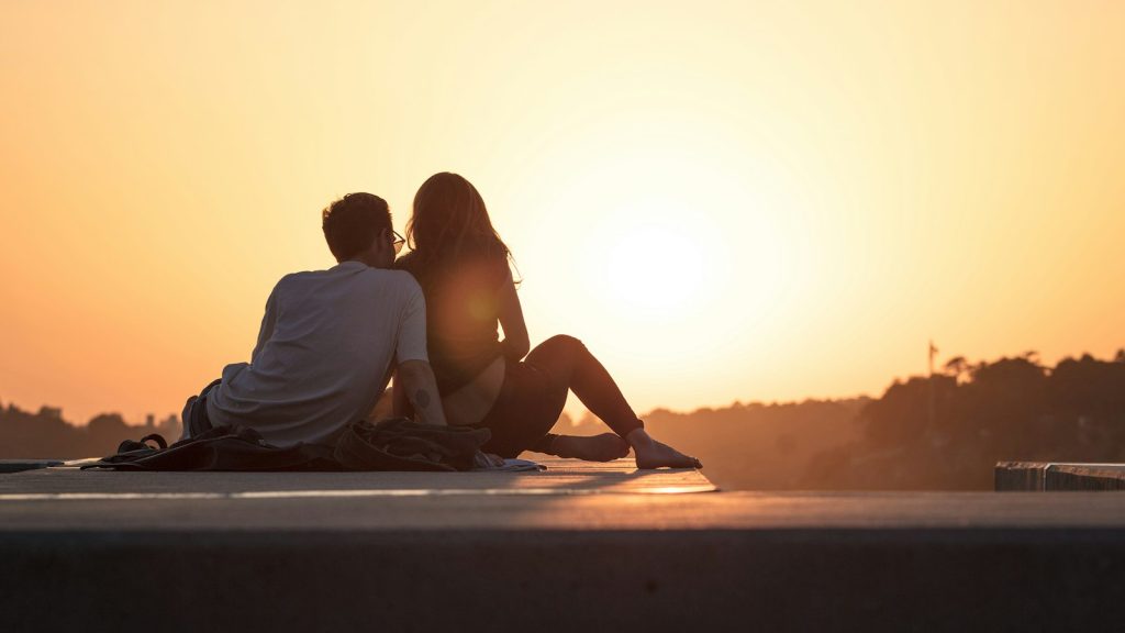 Couple sitting near trees at golden hour, weighing settling in a relationship