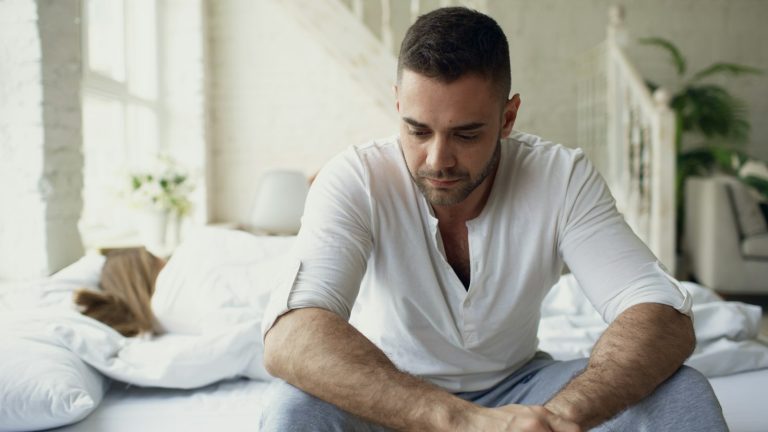 Man sitting on a bed looking down, a scene many know when a spouse is depressed