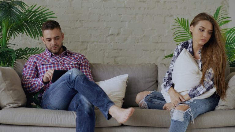 Couple sitting apart on a sofa after a hard talk, as partners who disagree about having kids often do