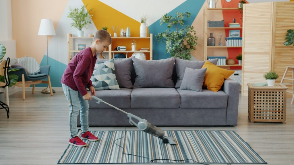 Young girl vacuuming a rug, one of the everyday chores for kids