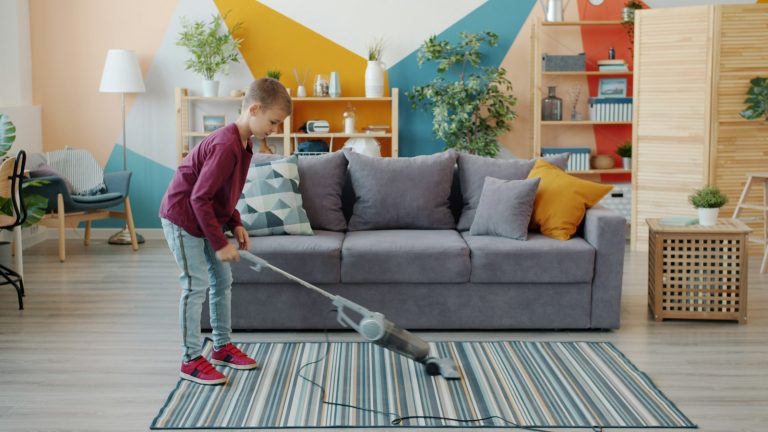Young girl vacuuming a rug, one of the everyday chores for kids