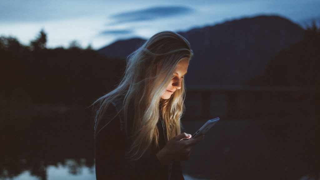 Woman reading messages on her phone by the water, the kind of quiet moment romance scams exploit