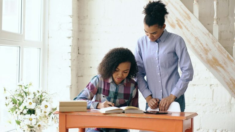 Woman helping a girl with schoolwork at a desk to avoid homework battles