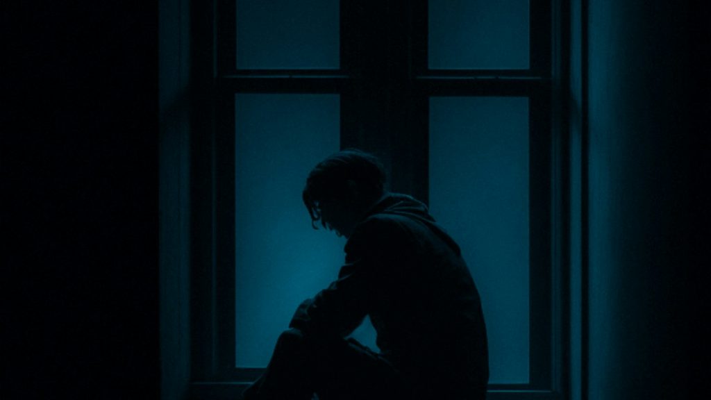 Young person sitting alone on a window sill, reflecting the inner side of divorce and teenagers
