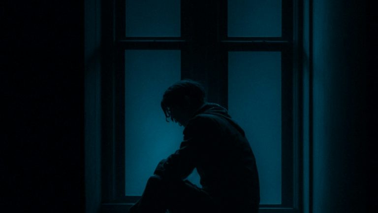 Young person sitting alone on a window sill, reflecting the inner side of divorce and teenagers